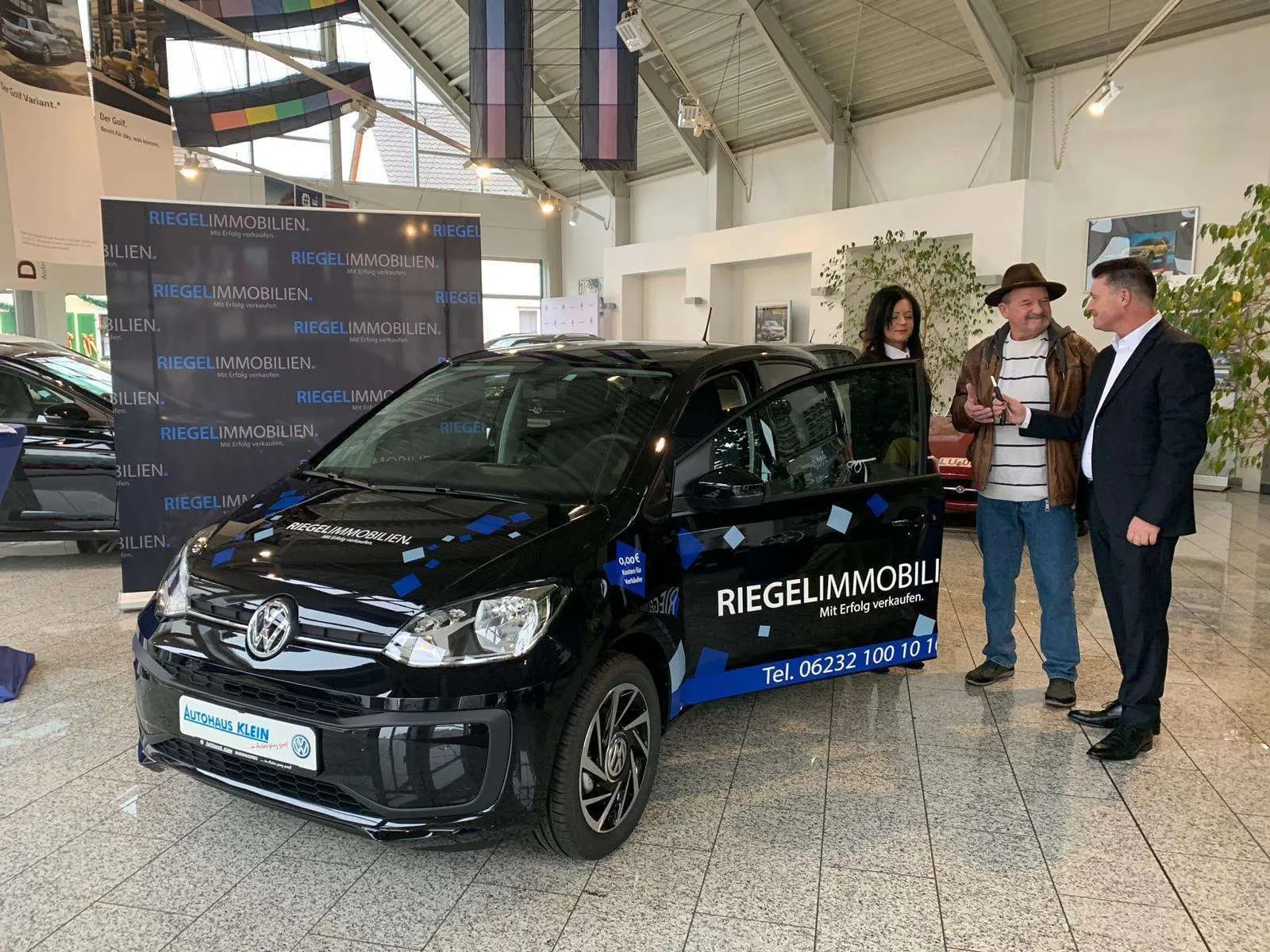 Fahrzeugübergabe eines gebrandeten VW up! mit RIEGEL-Immobilien-Beschriftung